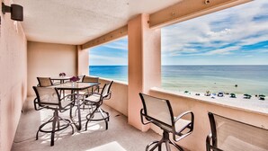 Un balcón con mesa y sillas, con vista a una playa con sombrillas.