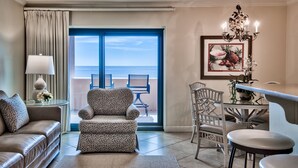 Habitación de hotel con sofá, sillón, mesa de comedor y sillas. Un ventanal grande ofrece vistas al mar.