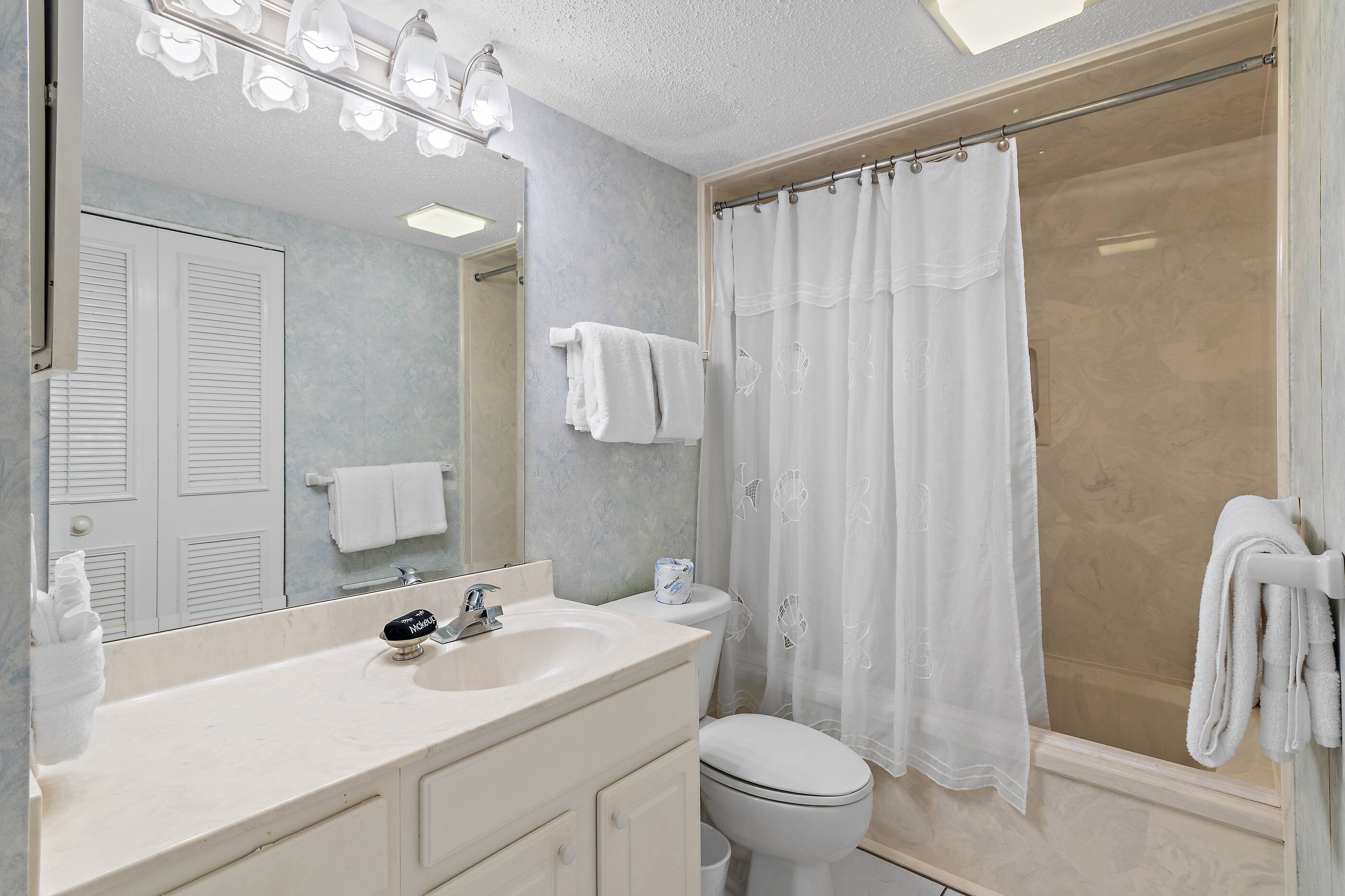 A bathroom with a sink, mirror, toilet, shower curtain, and towels.