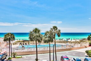 A beachfront hotel with a swimming pool, palm trees, and a view of the ocean.