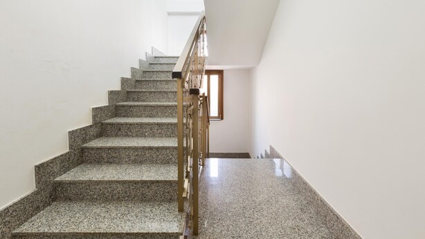 Una escalera de granito con barandilla de madera, que conduce a un rellano con una puerta.