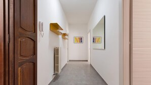 Un pasillo con una puerta de madera, un radiador y dos cuadros enmarcados en las paredes.