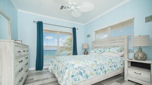 A bedroom with a bed, a dresser, a nightstand, a ceiling fan, and a window with curtains.