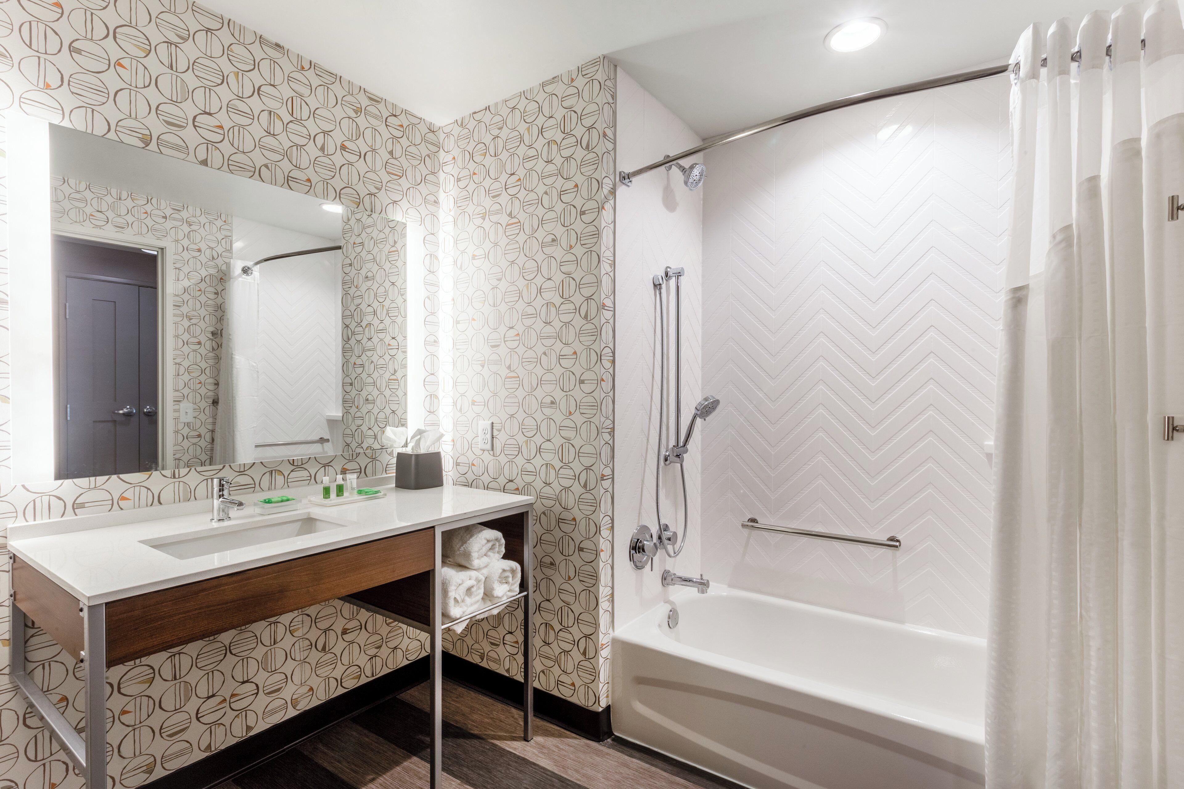 A modern bathroom with a white sink, mirror, shower, and herringbone-patterned walls.