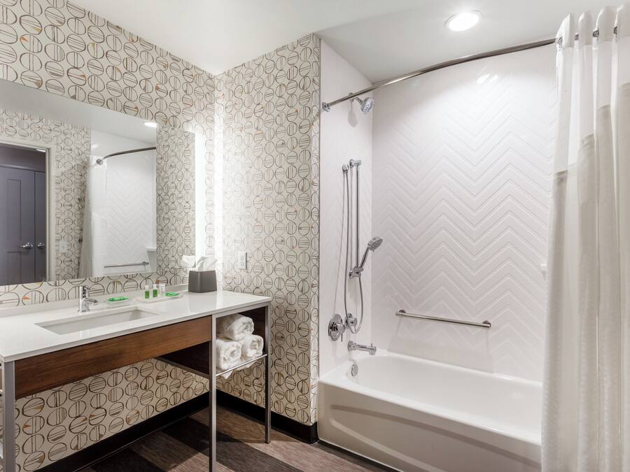 A modern bathroom with a white sink, mirror, shower, and herringbone-patterned walls.