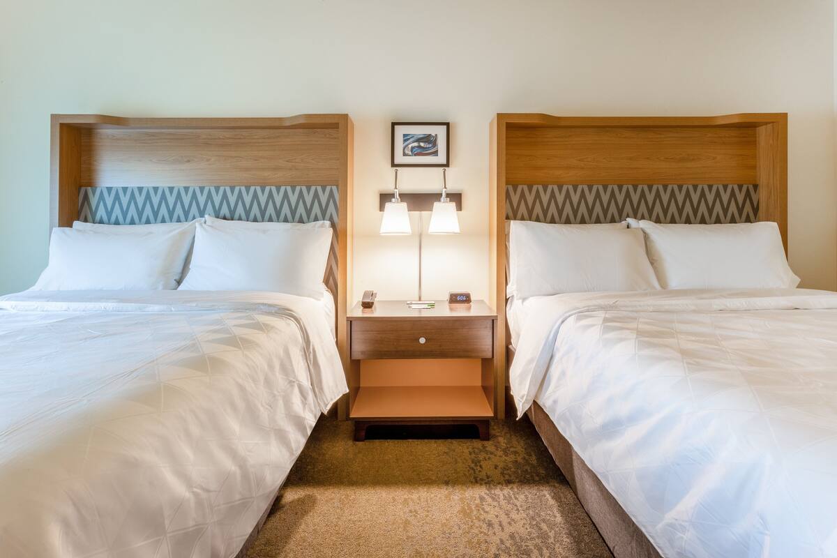 A hotel room with two beds, a nightstand with a lamp, and a framed picture on the wall.