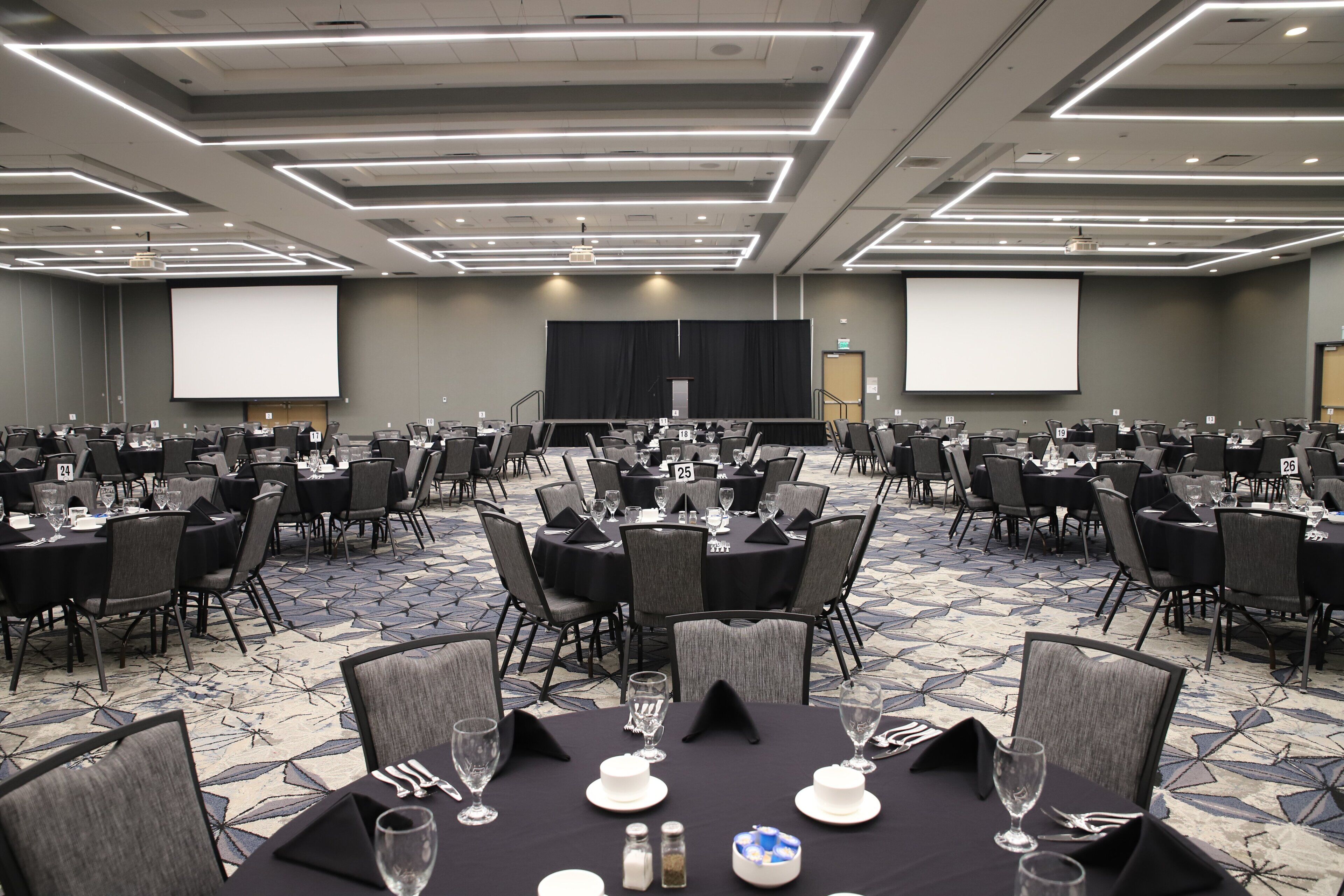 A conference room with multiple tables, chairs, and a large screen at the front.