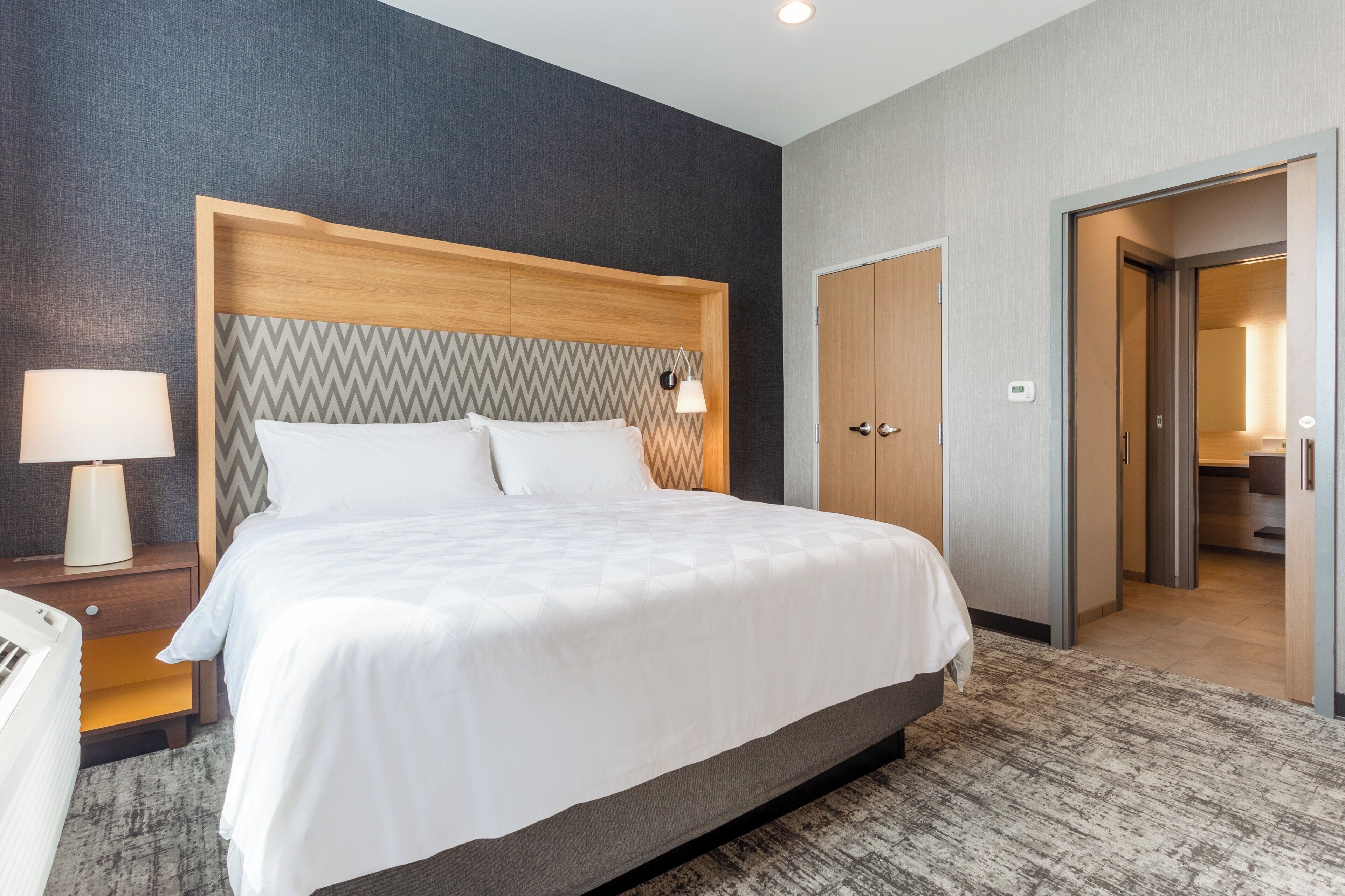 Une chambre d’hôtel avec un grand lit, une table de chevet avec une lampe, une armoire et une porte donnant sur une salle de bain.