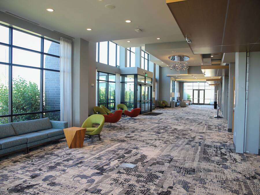 A spacious lobby with a patterned carpet, a long sofa, and several colorful chairs.