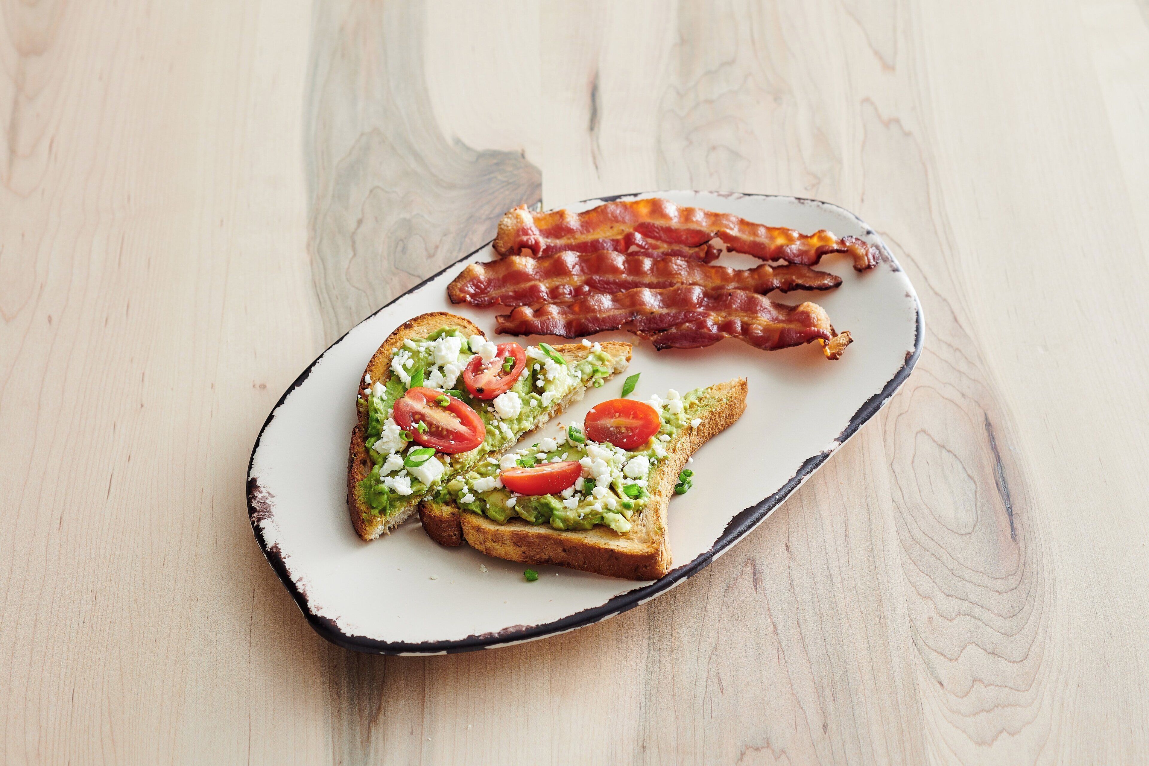 A plate with toast topped with avocado, tomatoes, and cheese, and a separate portion of bacon.