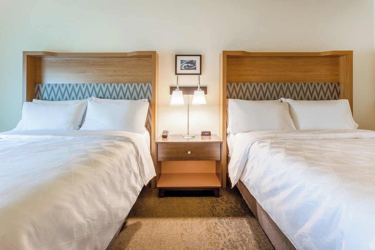 Een hotelkamer met twee bedden, een nachtkastje met een lamp en een lijst aan de muur.