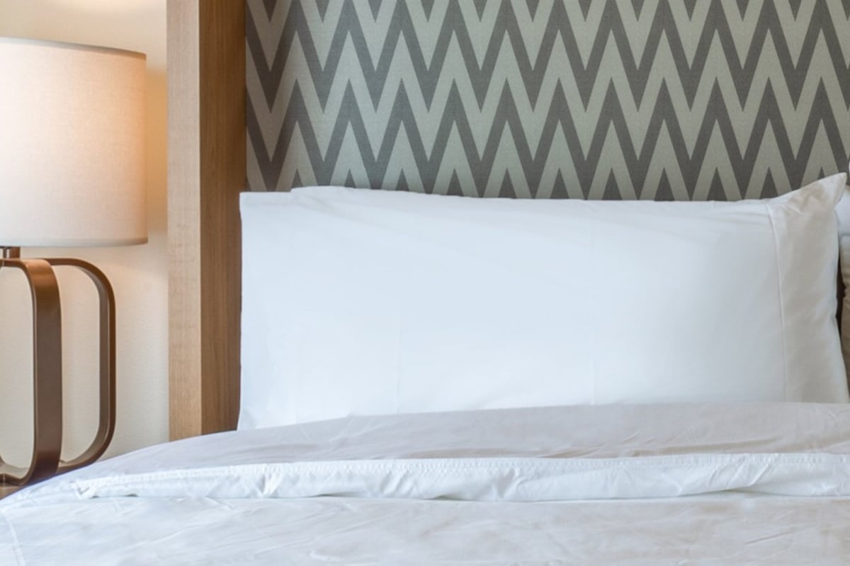 Een bed met witte beddengoed, een lamp en een muur met een chevronpatroon.