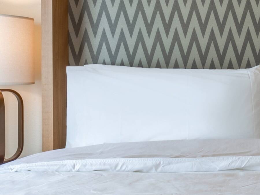Un lit avec une literie blanche, une lampe et un mur orné d’un motif en chevrons.