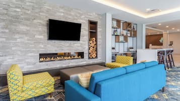 A modern living area with a fireplace, seating, and a flat-screen TV mounted on a stone wall.