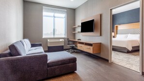 A modern hotel room with a sofa, desk, TV, and a bed. - Holiday Inn & Suites Cedar Falls - Waterloo Event Ctr by IHG (Cedar Falls)