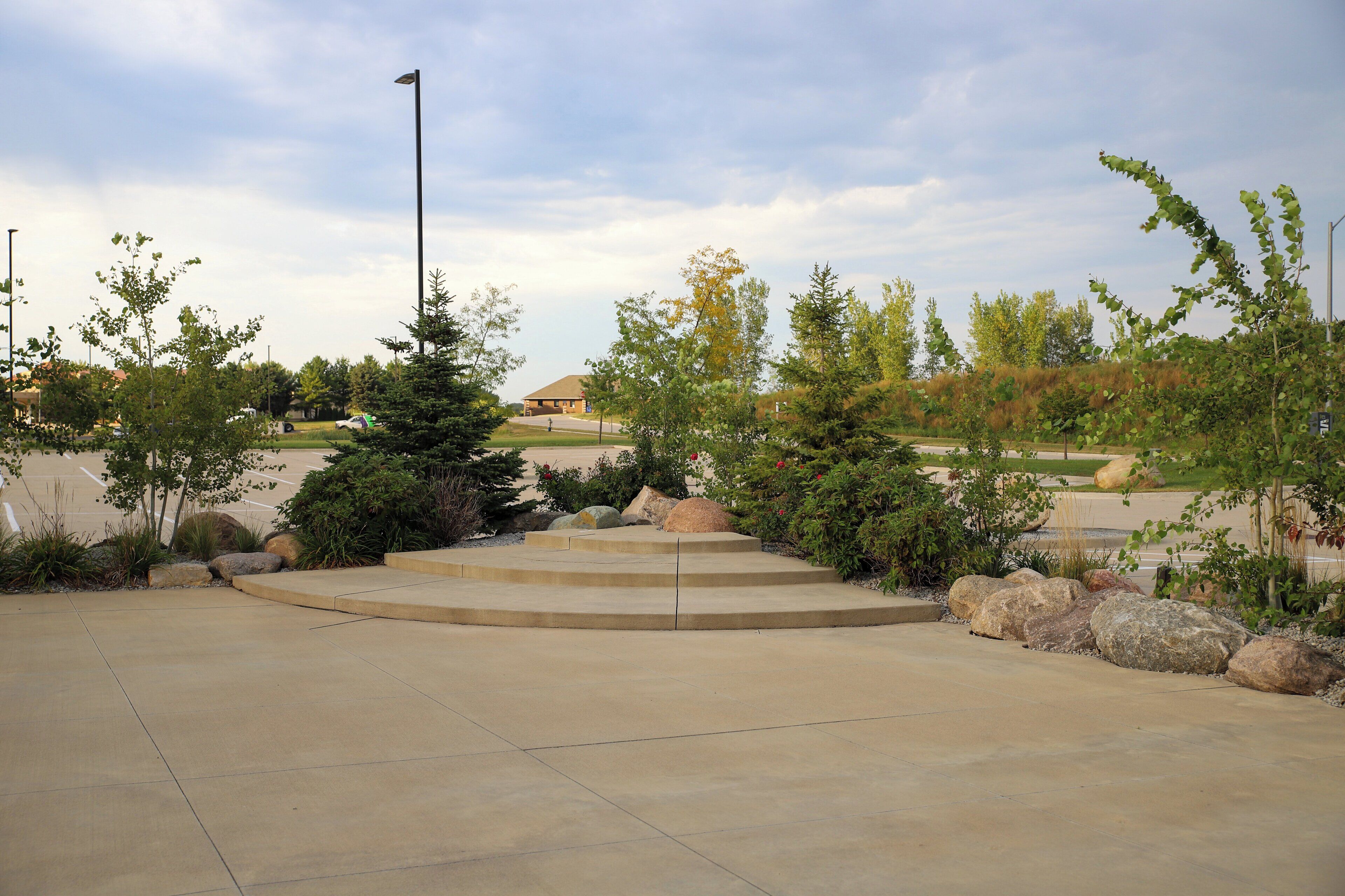 A paved outdoor area with steps leading to a building, surrounded by trees and rocks.