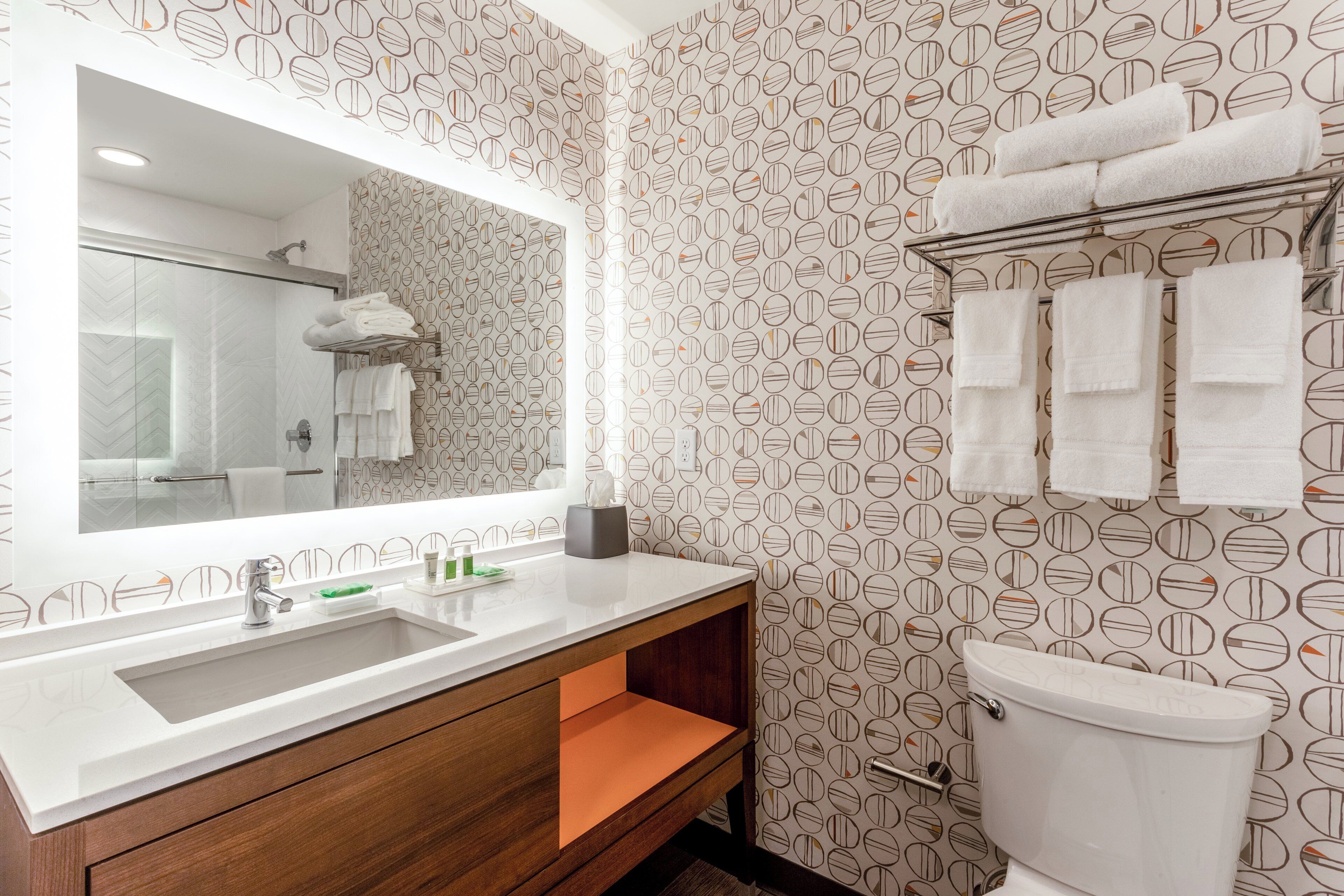 Une salle de bain avec un grand miroir, un lavabo, des toilettes et un porte-serviettes.