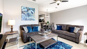 A modern living room with two grey sofas, a coffee table, a side table, and a blue abstract painting on the wall.