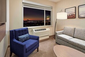 Una sala de estar moderna con un sillón azul, un sofá gris, un ventanal con vistas a la ciudad y una lámpara de pie.