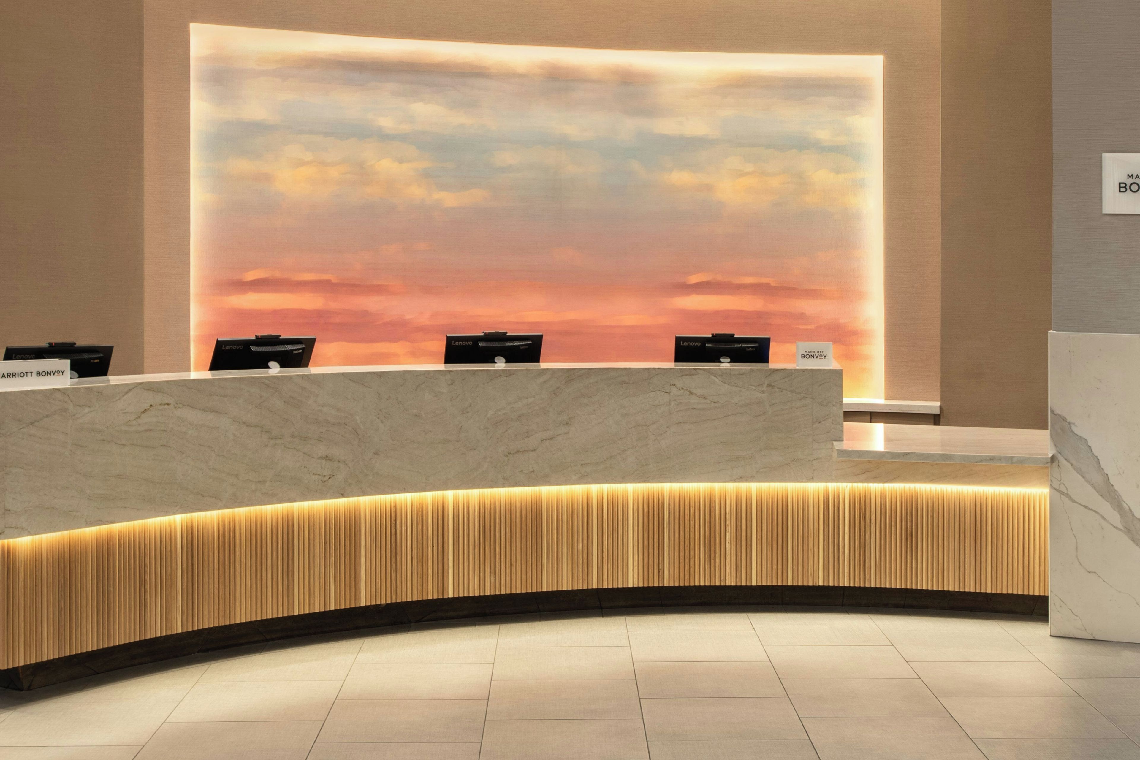 Un comptoir d’accueil doté d’un plateau en marbre et d’un panneau décoratif en bois, placé devant un grand mur offrant une vue sur le coucher de soleil.