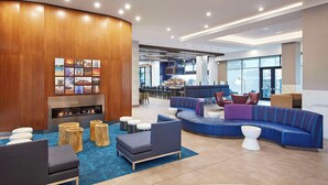 A modern lobby with a curved wooden wall, a fireplace, and a seating area with sofas and round tables. - Anaheim Resort Suites (Anaheim)