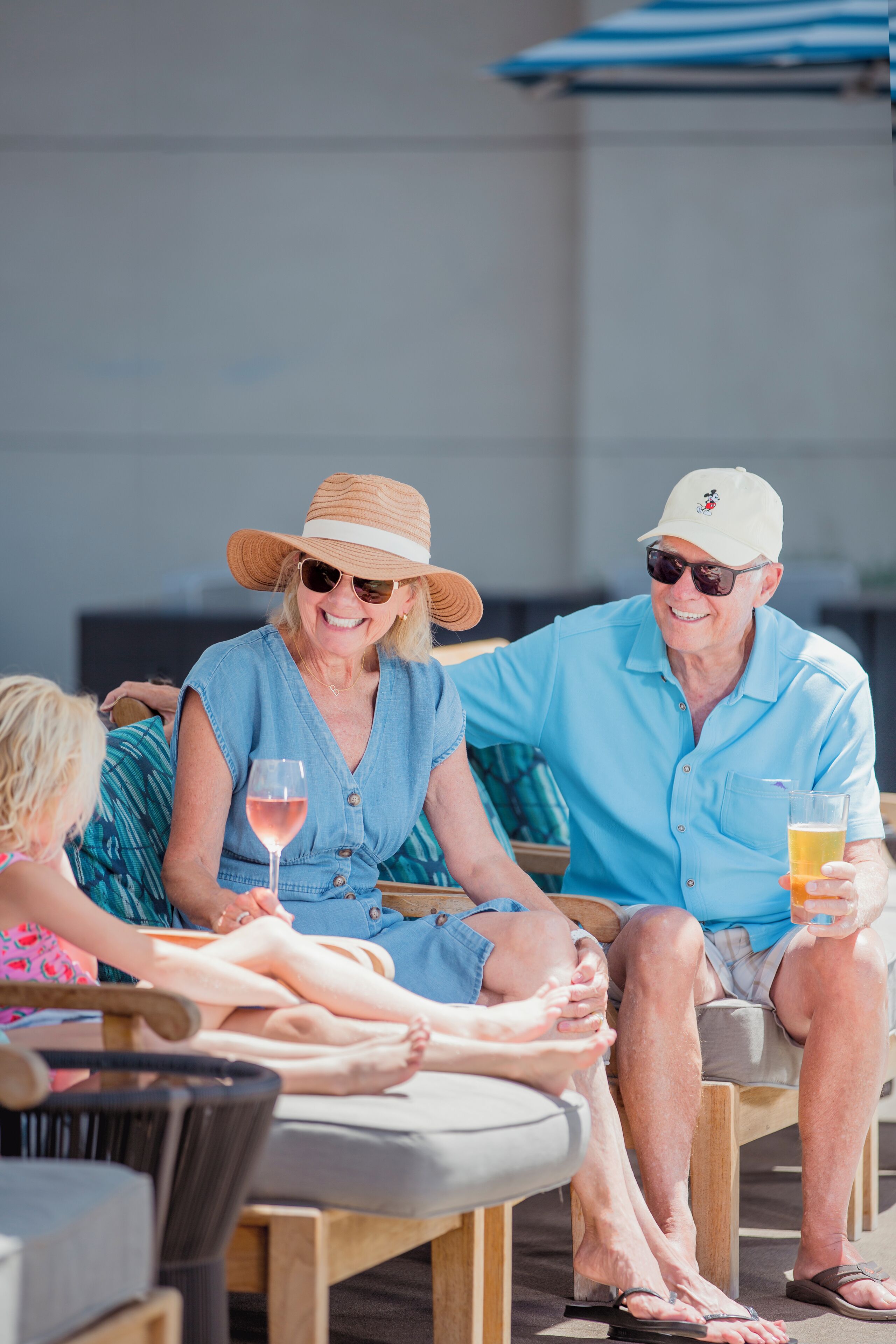 A group of people sitting on outdoor lounge chairs, with a pool and umbrellas in the background.