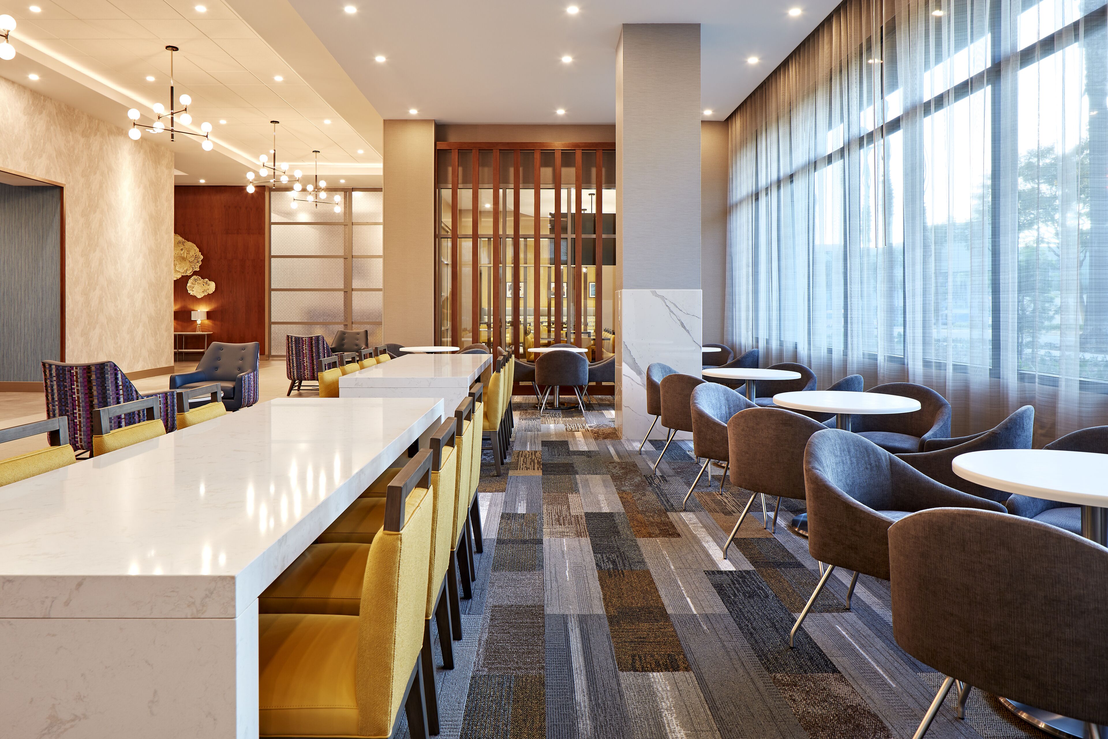 A modern hotel lobby with a long reception desk, comfortable seating, and large windows providing natural light.