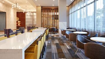 A modern hotel lobby with a long reception desk, comfortable seating, and large windows providing natural light.