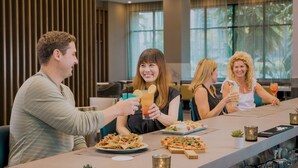 A group of people dining at a restaurant with a bar area, large windows, and modern interior design. - Anaheim Resort Suites (Anaheim)