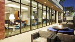 An outdoor seating area with wicker furniture, a fire pit, and glass walls offering views of the interior. - Anaheim Resort Suites (Anaheim)