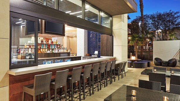 A bar area with a long counter, multiple bar stools, and a seating area with tables and chairs. - Anaheim Resort Suites (Anaheim)
