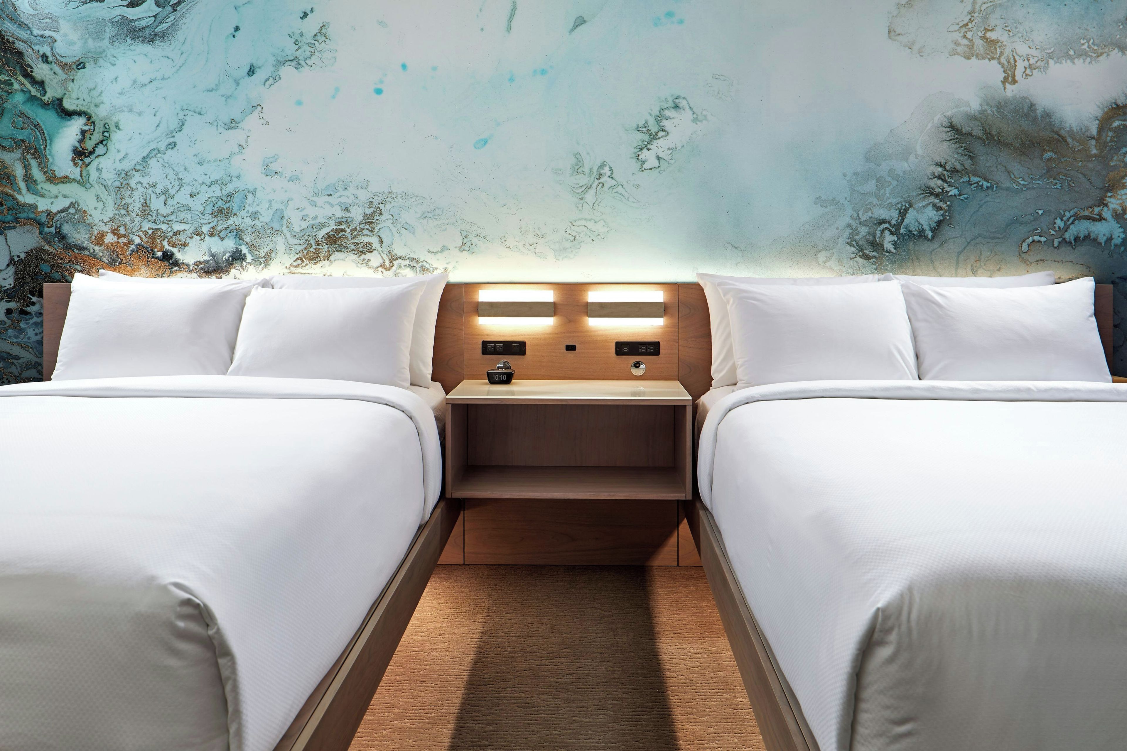 A double room with two beds, a nightstand with a clock, and a textured wall.