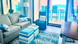 Un salon comprenant un canapé, des poufs, une lampe et une vue sur l’océan grâce à de grandes fenêtres.