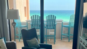 Un balcon avec des chaises et une table turquoise, donnant sur une mer aux eaux turquoise.