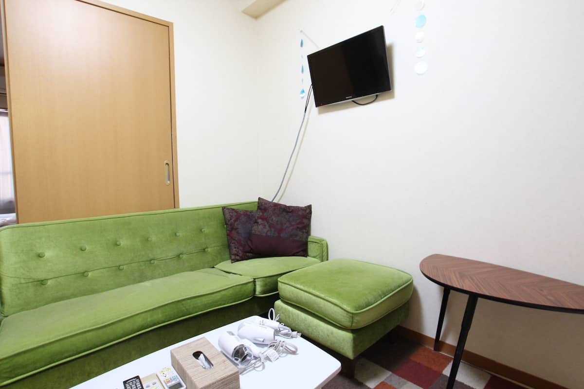 A green sofa, a small table, a flat-screen TV, and a door in a room.