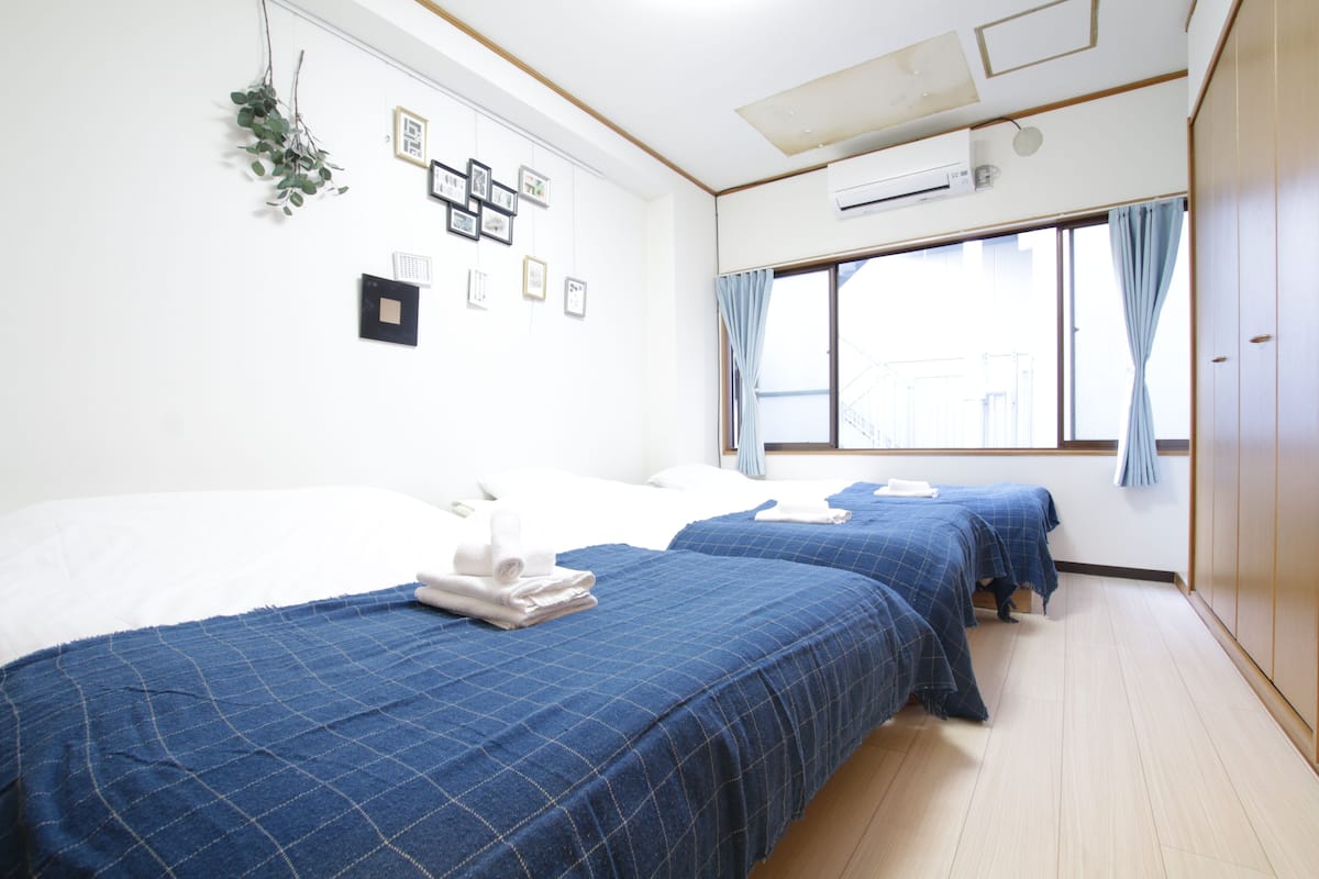 A hotel room with two beds, a large window with curtains, a wall-mounted air conditioner, and framed pictures.