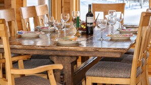 Ein Esszimmer mit einem Holztisch, der mit Tellern, Gläsern und einer Weinflasche gedeckt ist, umgeben von Stühlen mit gepolsterten Sitzflächen.
