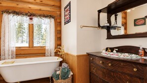 Ein traditionelles Holz-Blockhaus-Badezimmer mit einer Badewanne auf Füßen, einem Holzwaschtisch mit mehreren Schubladen und einem großen Spiegel über dem Waschbecken.