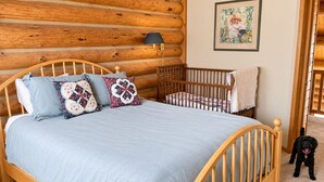 Ein Schlafzimmer mit einem hölzernen Bett, einem Babybett, einem Hund und einem gerahmten Bild an der Wand.