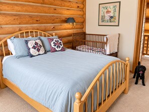 Un dormitorio con una cama de madera, una cuna, un perro y un cuadro en la pared.