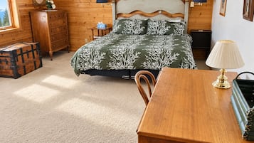 A wooden room with a bed, dresser, and a table with a lamp.