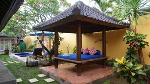 A gazebo with a blue cushioned bench and a small pool in the background.