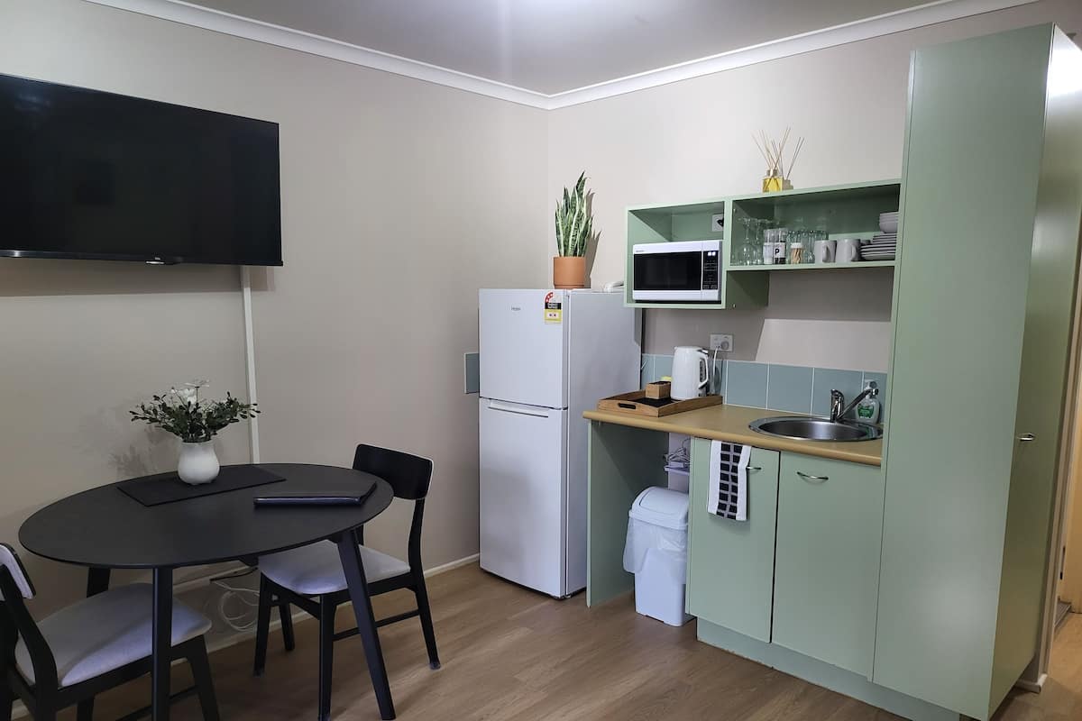 Een compacte keuken met een koelkast, magnetron en een klein eethoekje met een tafel en stoelen.
