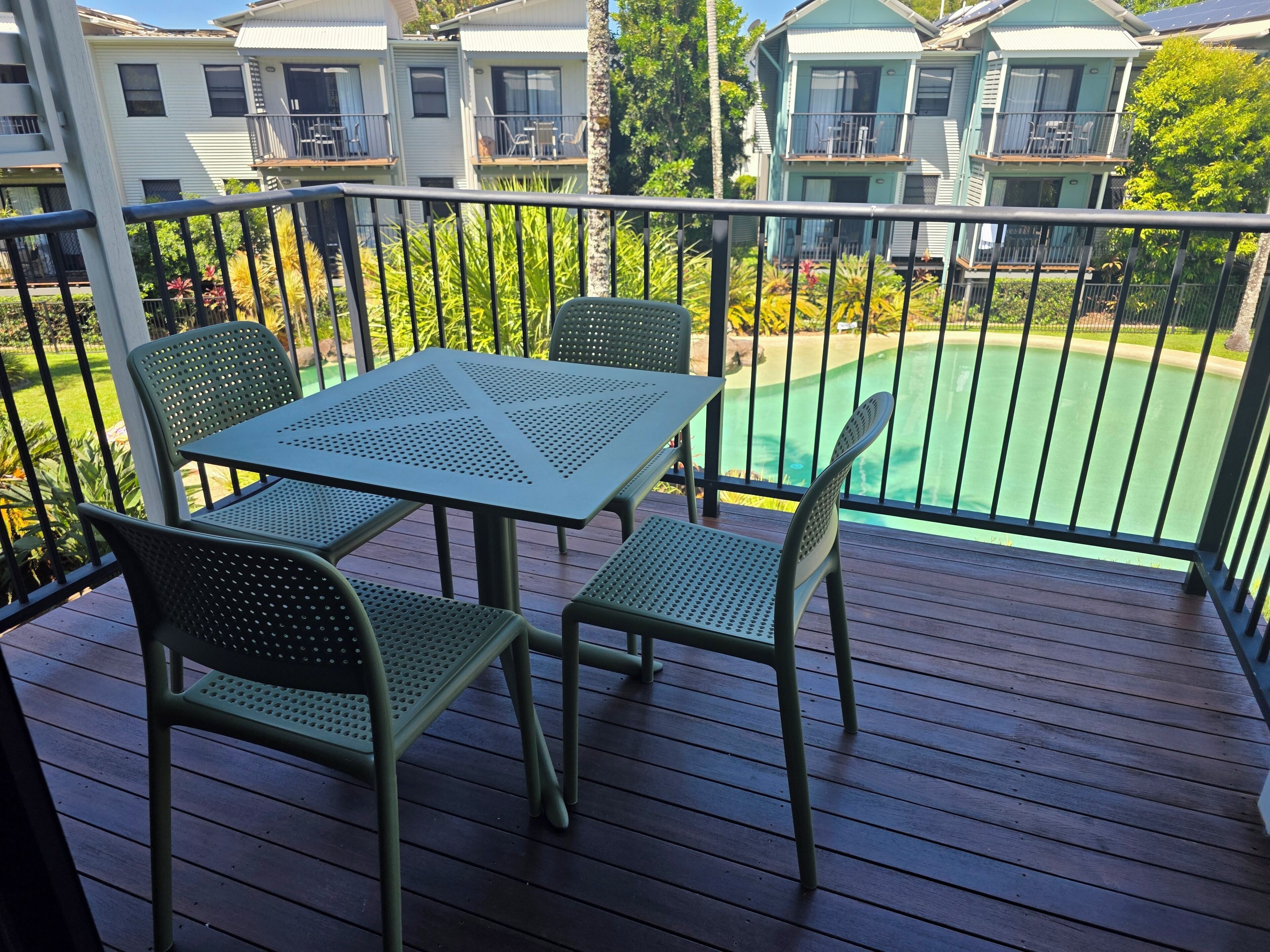 Varanda com mesa e cadeiras, vista para uma piscina e edifícios residenciais.