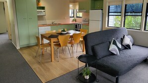 A compact living space with a dining area, kitchenette, and a sofa with a view of greenery. - Noosa Holiday Accommodation (Tewantin)