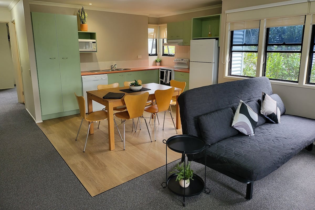 Een gezellig, compacte leefruimte met een eethoek, een kitchenette en een sofa met kussens.