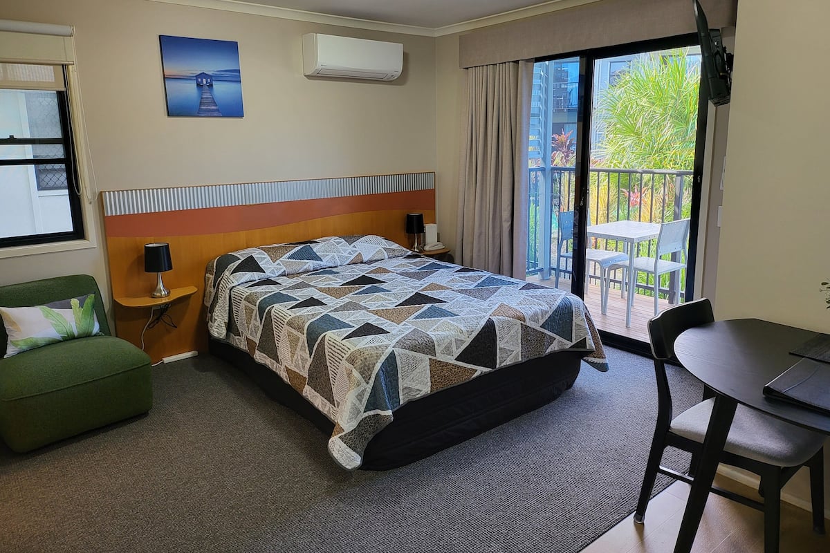 Hotelkamer met een bed, bureau, stoel, groene fauteuil, airconditioning, schilderij en balkon met tafel en stoelen.