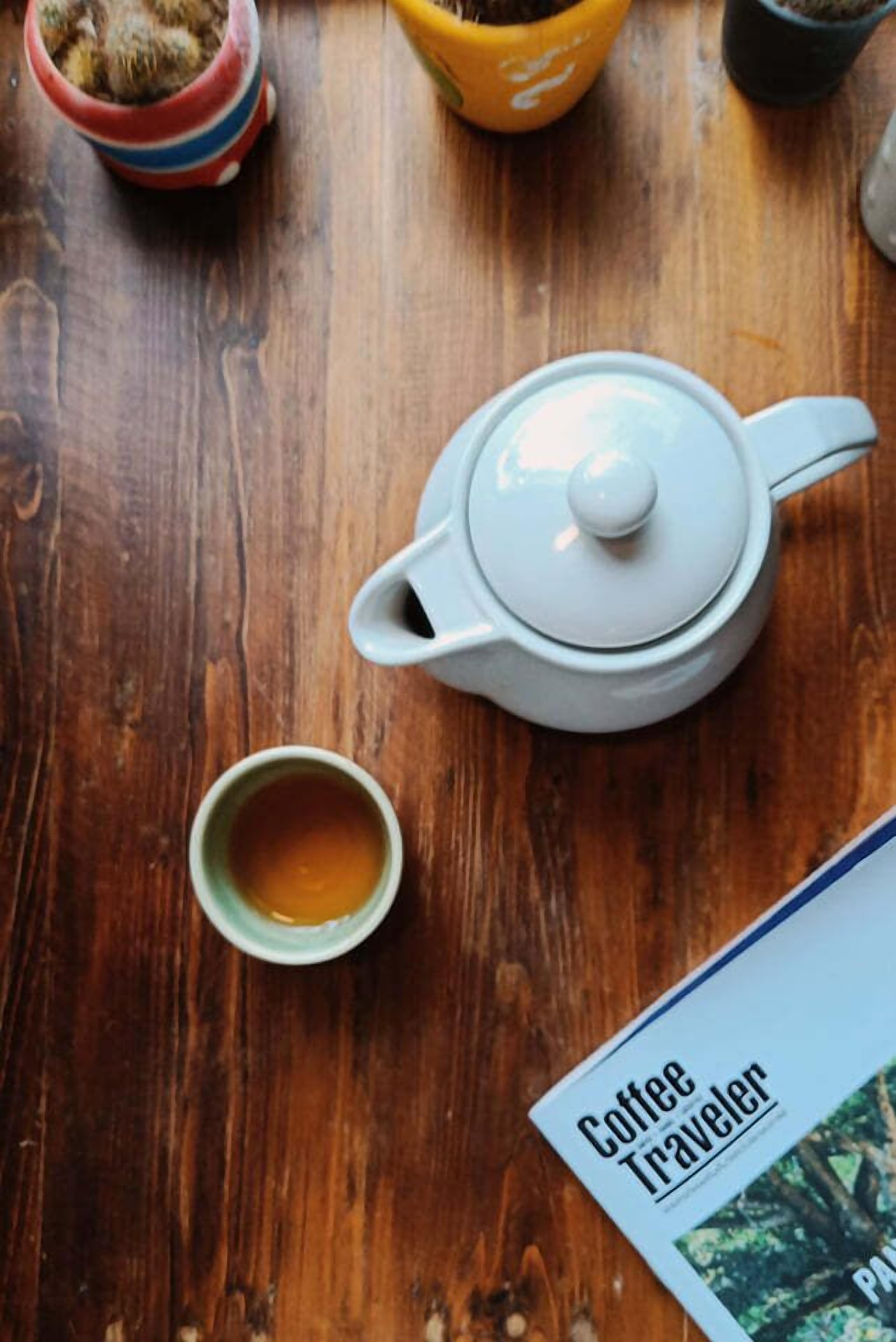 A wooden table with a white teapot, a green cup of tea, and a magazine titled "Coffee Traveler".