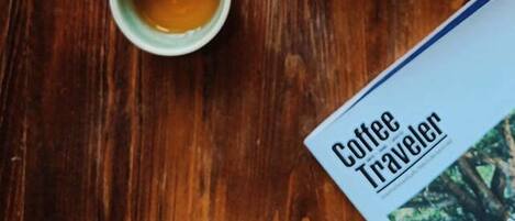 A wooden table with a white teapot, a green cup of tea, and a magazine titled "Coffee Traveler".