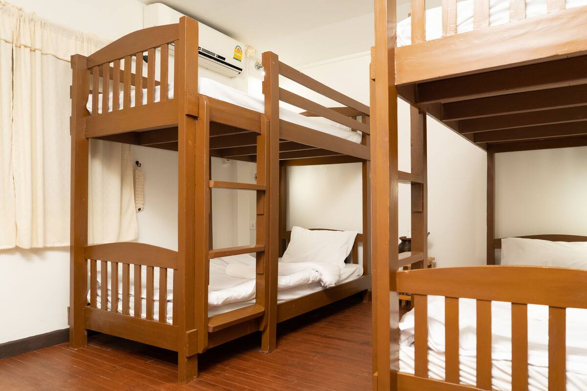A room with bunk beds, a wooden floor, and a white wall with a window.